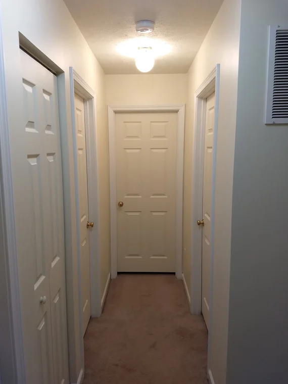 This is an image from Roman Paint Pros company, located in Penn Hills, PA. The image is a freshly painted interior hallway with cream walls, white trim, and six-panel doors, completed by Roman Paint Pros residential painting service.