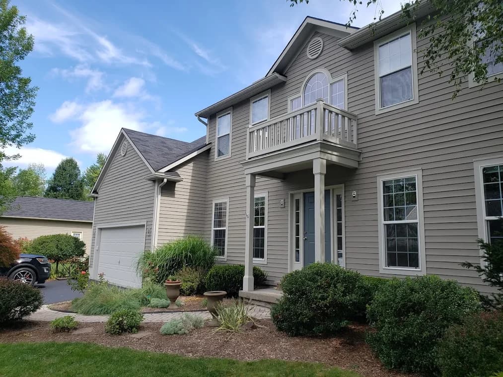 This is an image from Braun's Painting, LLC, located in New York. The image shows a freshly painted two-story suburban home with beige siding, white trim, and a clean landscaped front walkway.
