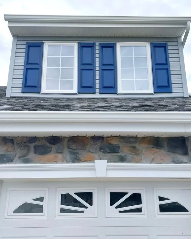 This is an image from Clean Lines Painting & Powerwashing of New Jersey, the image is a upper view of a home exterior with gray siding, stone details, and freshly painted blue shutters, completed by Clean Lines Painting + Powerwashing for a polished appearance.
