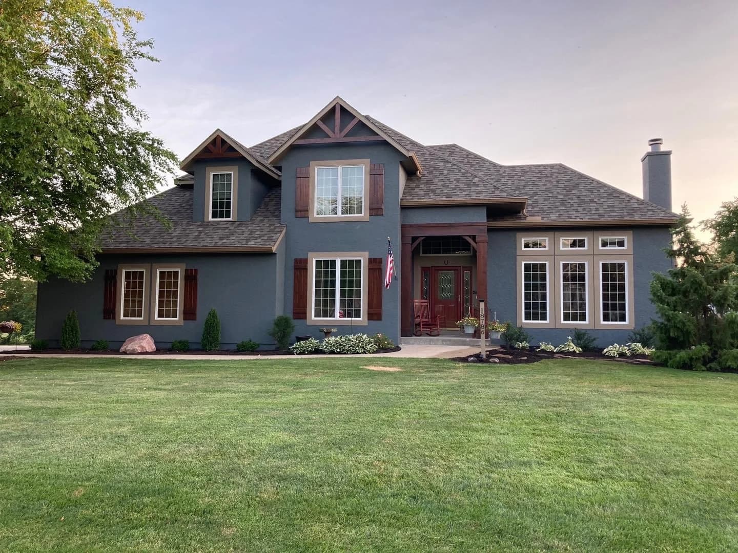 This is an image from Brogan Painting & Remodeling. The image shows a dark blue stucco home with newly painted trim and wood shutter accents.