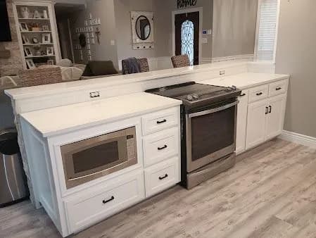 "This is an image from James Painting & Remodeling, located in Texas. The photo shows a remodeled kitchen area with white cabinetry, a built-in microwave, stainless steel stove, and light wood flooring."