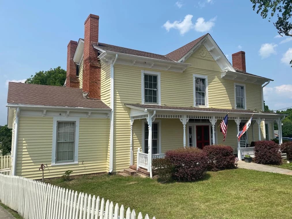 Exterior painting project by Hansell Painting Co in Durham, NC. The image shows a yellow historic home with white trim, porches, and brick chimneys.