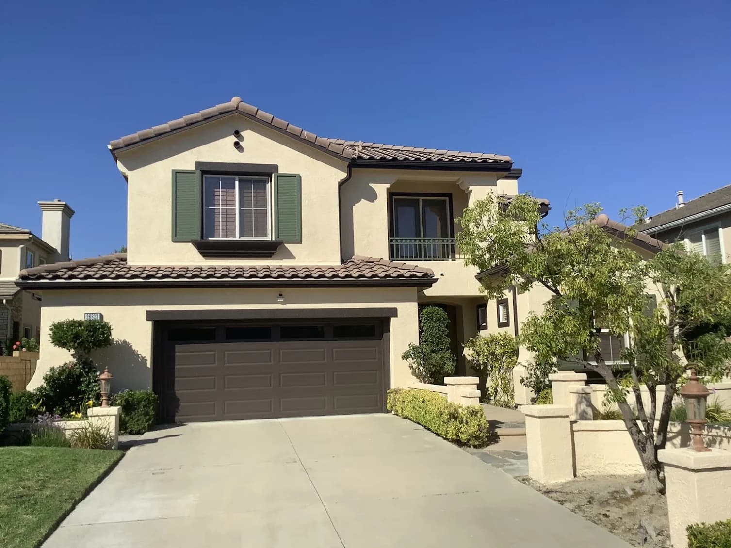 This is an image from ALLBRiGHT Painting, located in California. The image is from ALLBRiGHT Painting and shows exterior painting on a two-story tan home with green shutters and a dark brown garage door.