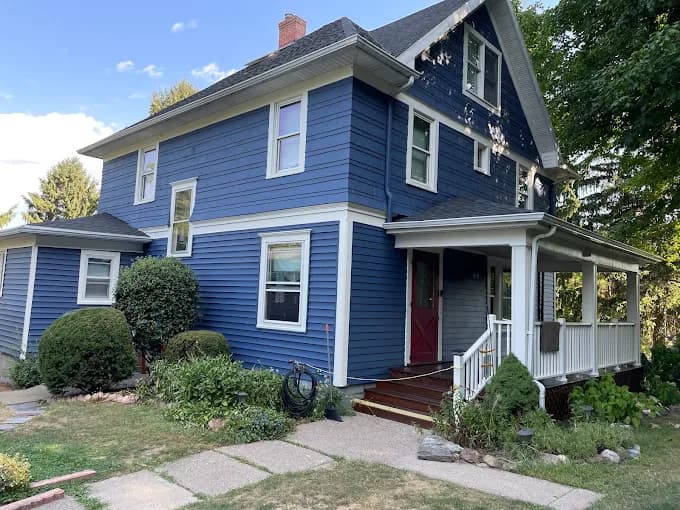 This is an image from Monarch Painting, located in New York. The exterior image shows a freshly painted blue two-story home with white trim, a covered porch, and surrounding landscaping.