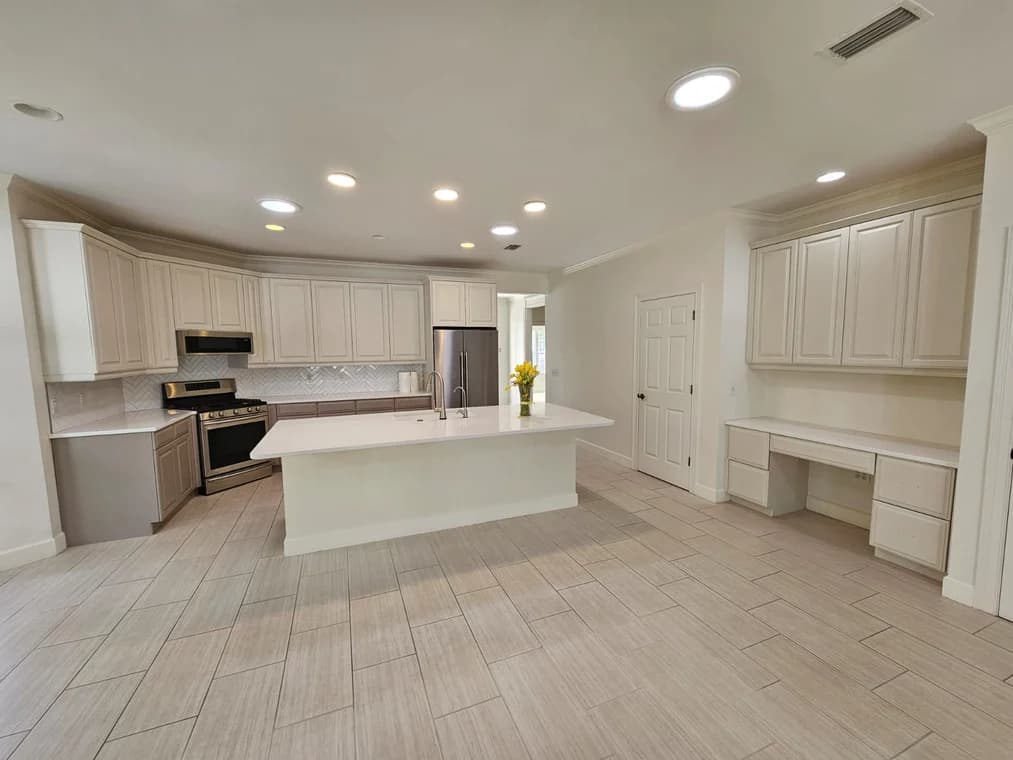 This is an image from HH Painting company, located in Gainesville, FL. The image is a modern kitchen with freshly painted white cabinets, large island, and built-in desk area with light tile flooring