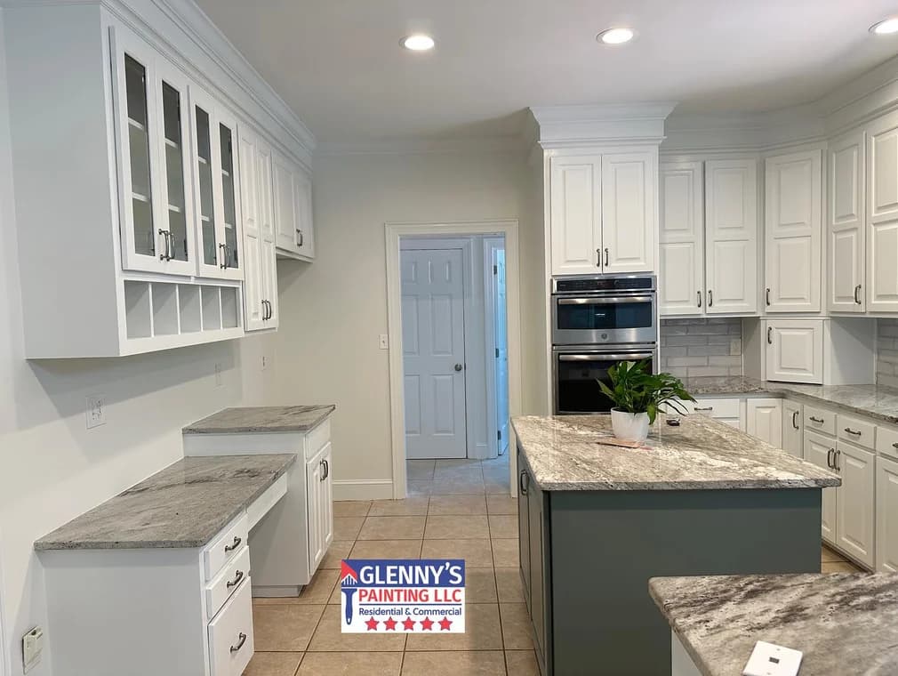 Cabinet painting project by Glenny's Painting LLC in Charlotte, NC. The image shows white kitchen cabinets, stone counters, and a dark green island.