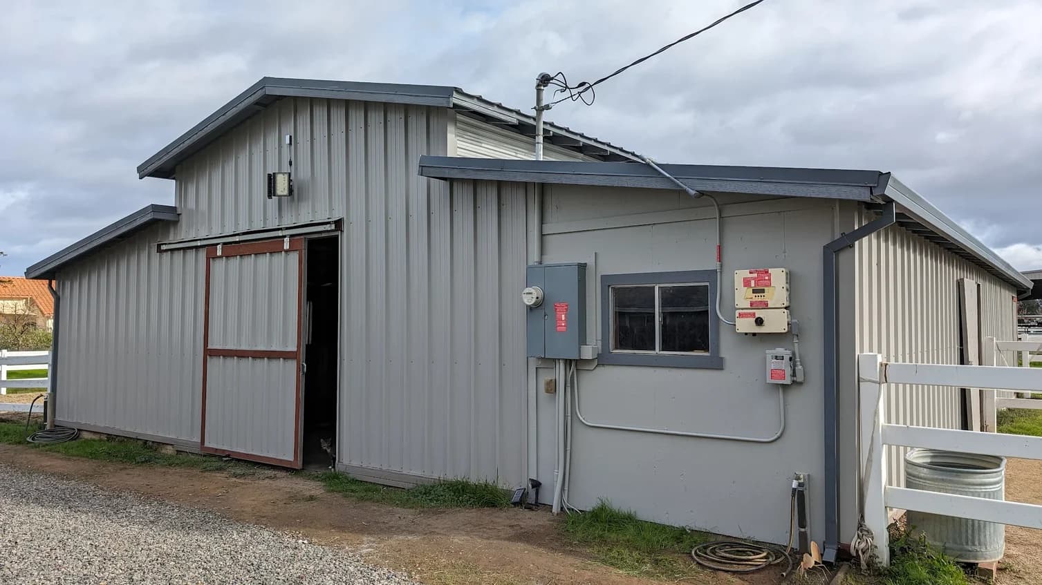 This is an image from Brooks Painting, located in California. The image is from Brooks Painting and shows exterior painting on a large gray metal barn with sliding doors and utility panels along the side.