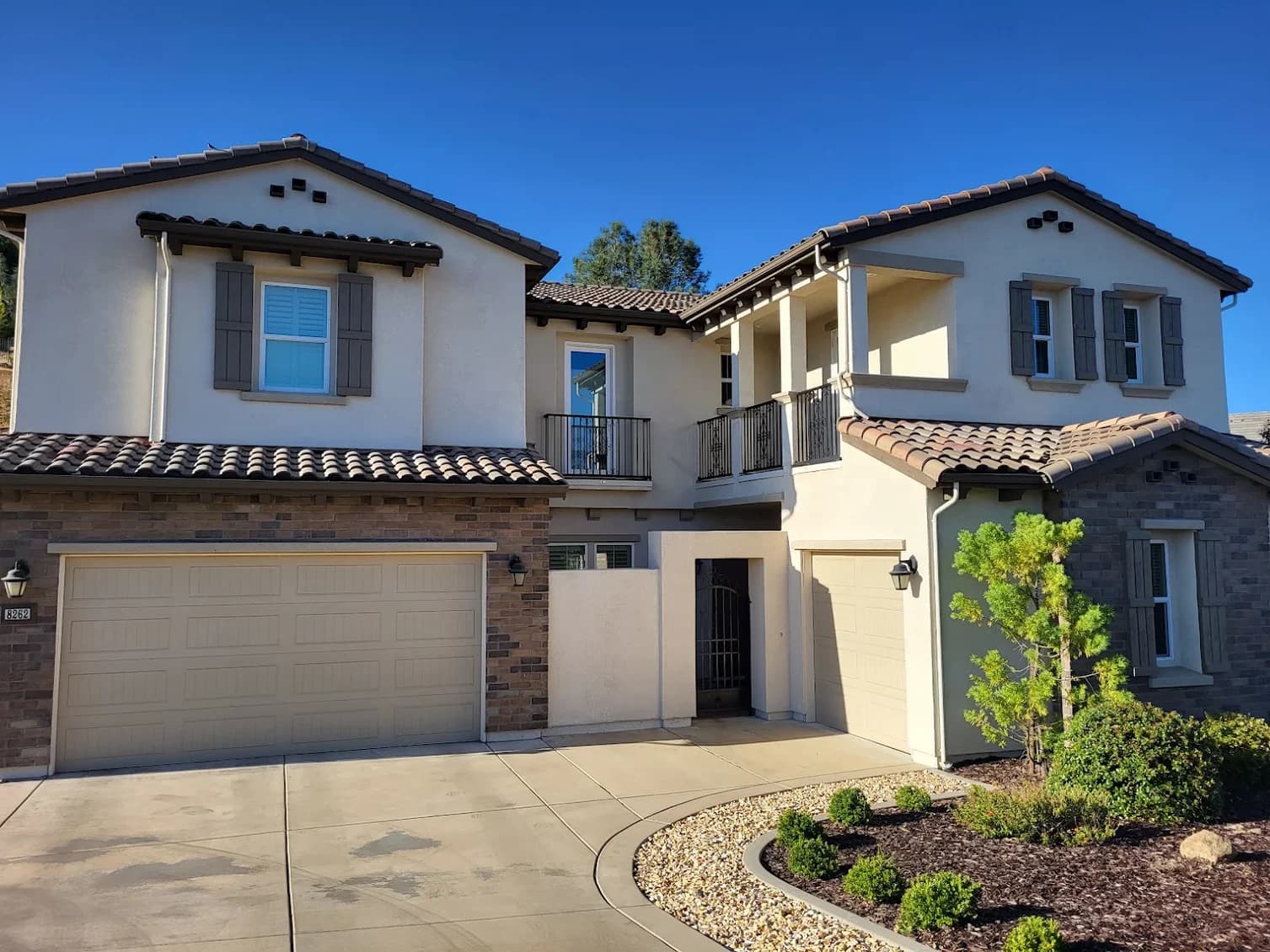 This is an image from Brooks Painting, located in California. The image is from Brooks Painting and shows exterior painting on a two-story stucco home with stone accents, decorative shutters, and a landscaped front yard.