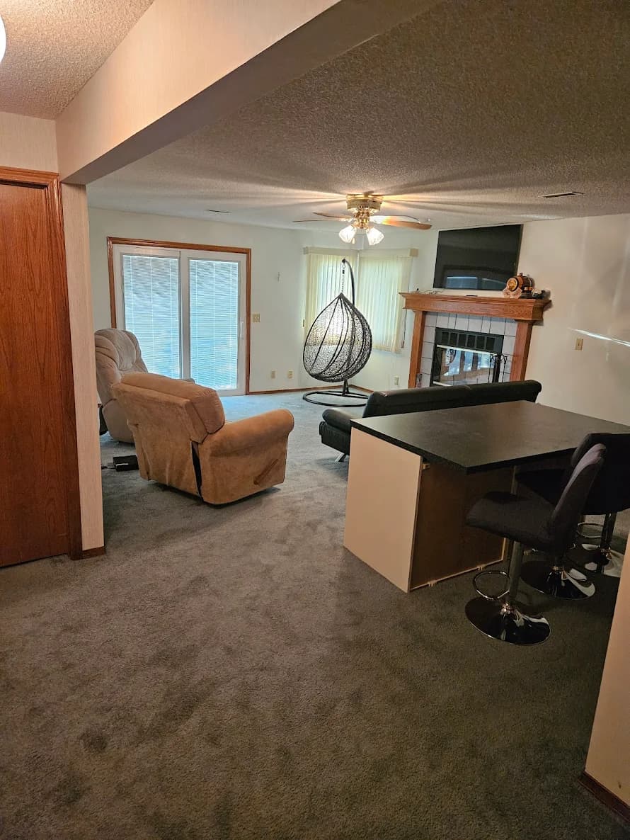 This is an image from 360 Painting of Wichita. The image shows a basement living area with updated painted walls that brighten the space around the carpet and fireplace.