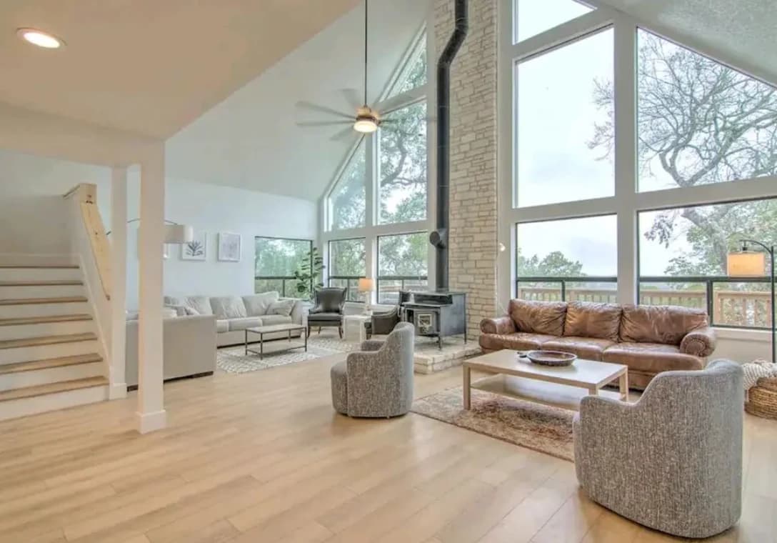 "This is an image from Paramo Painting, located in Texas. The living room features a tall vaulted ceiling, floor-to-ceiling windows, a stone fireplace, and modern neutral furnishings."