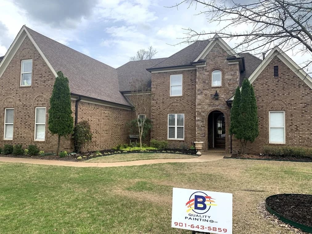 Exterior painting by B Quality Painting LLC in Arlington, Tennessee. The image shows a two-story brick home with dark trim and a company yard sign.