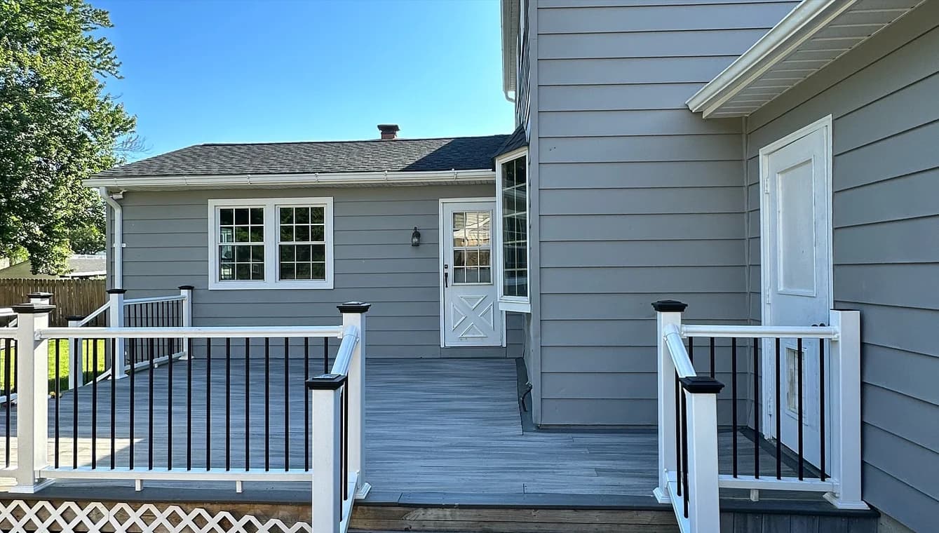 Back deck of a home with gray siding and white trim, featuring black and white railing after repainting.