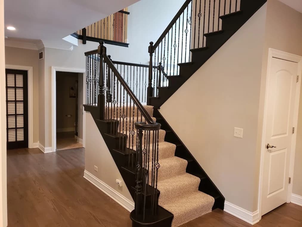 Interior trim painting by Always Perfect Painters in St. Charles, Illinois. The image shows dark stair rails and posts beside light walls and carpet.