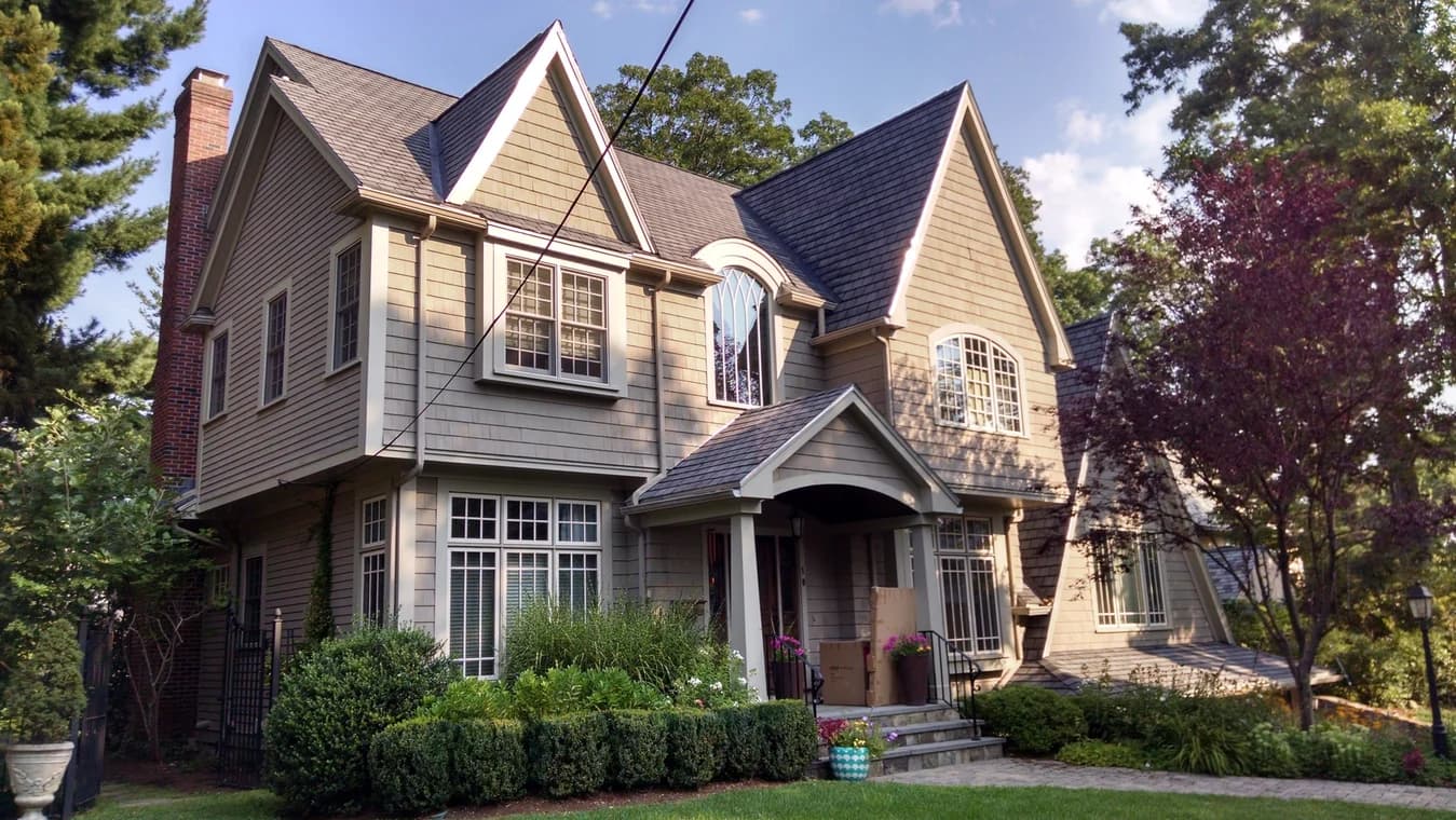This is an image from Catchlight Painting, located in Massachusetts. It shows a beige-colored home with gray roofing, tall gables, and carefully maintained landscaping.