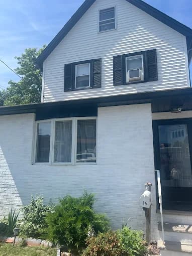 This is an image from Premier Painting Pros, located in New York. The exterior photo shows a white-painted two-story home with black shutters, a black entry door, and small garden plants near the front steps.