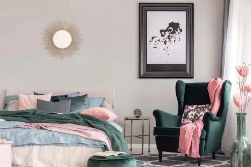 This is an image from The Woodlands Paint Doctor, located in Texas. The interior shot displays a decorated bedroom with muted wall colors, a green armchair, a pink throw blanket, and framed wall art.