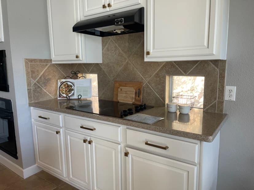 This is an image from CertaPro Painters of San Antonio, located in Texas. The kitchen photo shows white cabinets with brass hardware, a tiled backsplash, and a built-in cooktop.