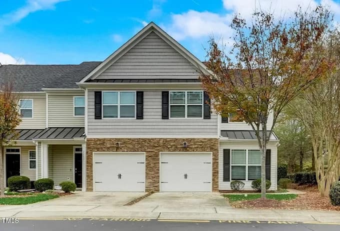 Exterior painting project by Socaz Painting in Raleigh, NC. The image shows a gray townhome with stone accents, black shutters, and two white garage doors.