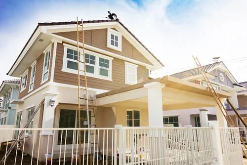 This is an image from Ponderosa Painting LLC, located in  Louisiana. The photo shows a two-story home being painted with ladders set up against the tan and white exterior, capturing the company's residential painting work in progress.