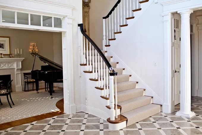 This is an image from Whitehouse Residential & Commercial Painting, located in Kentucky. The image shows a freshly painted interior staircase and foyer with white trim, decorative columns, patterned flooring, and a bright, elegant finish.