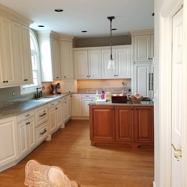 This is an image from Donovan’s Painting, located in Maryland. The photo shows a bright kitchen with white cabinets, a central island with wood finish, granite countertops, and hardwood flooring.