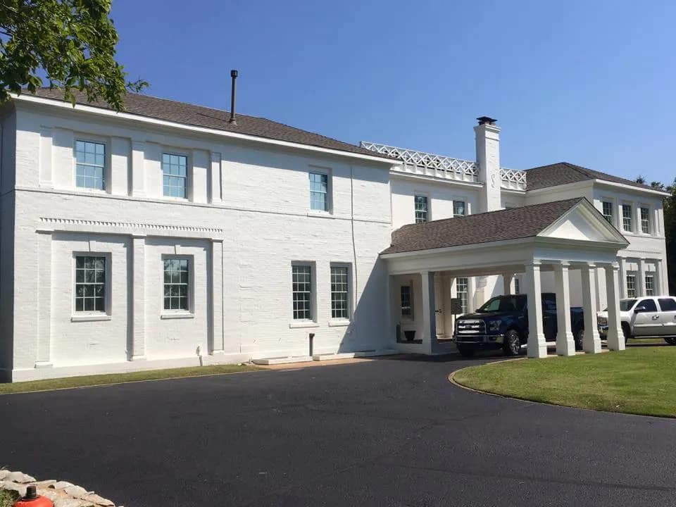 This is an image from Legacy Painting, located in Edmond, Oklahoma. The picture features a freshly painted two-story white brick home with tall columns, a blacktop driveway, and vehicles parked in front.
