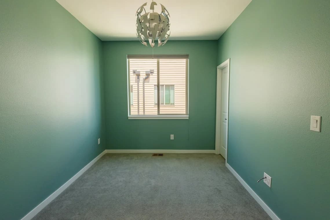 This is an image from Paint Denver company, located in Denver, CO The image is a freshly painted small bedroom with seafoam green walls, white trim, and modern ceiling light fixture by Paint Denver interior painters