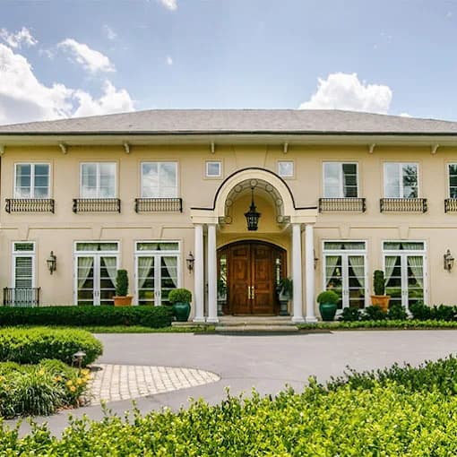 This is an image from Whitehouse Residential & Commercial Painting, located in Kentucky. The image shows a large luxury home exterior with freshly painted light-colored stucco, arched entryway, symmetrical windows, and manicured landscaping.