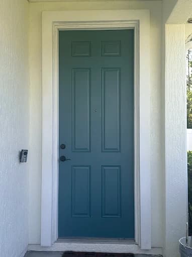 This is an image from Rockstar Painting, Inc. company, located inJacksonville, FL. The image is a freshly painted teal front door with white trim on textured exterior wall—residential entryway project by Rockstar Painting Inc.