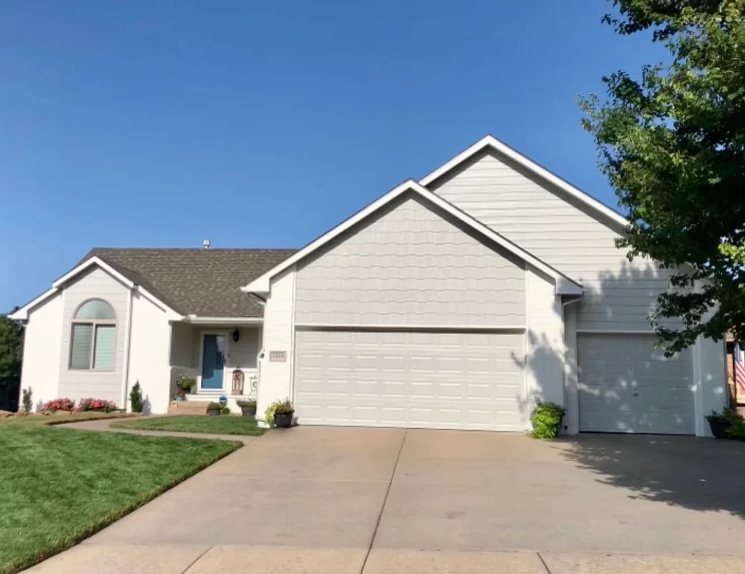 This is an image from CertaPro Painters of Wichita East KS. The image is a single-story white home in Wichita KS with fresh exterior paint and a blue front door.