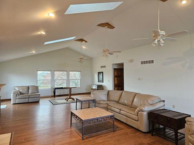 This is an image from Hearts & Hands Painting, located in Kentucky. The image shows a professionally painted living room interior with vaulted ceilings, skylights, white walls, hardwood floors, and a bright open layout.