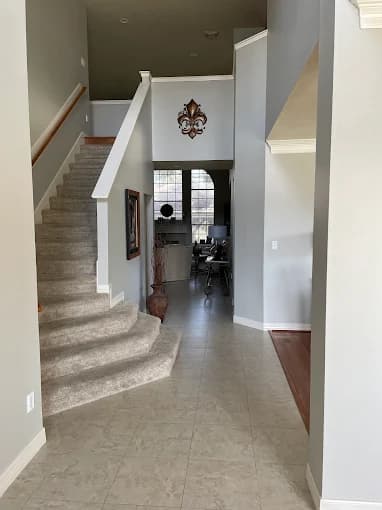 This is an image from DABS Painting, located in Texas. The image shows a freshly painted interior hallway with light gray walls, tiled flooring, and a staircase leading to the second floor.