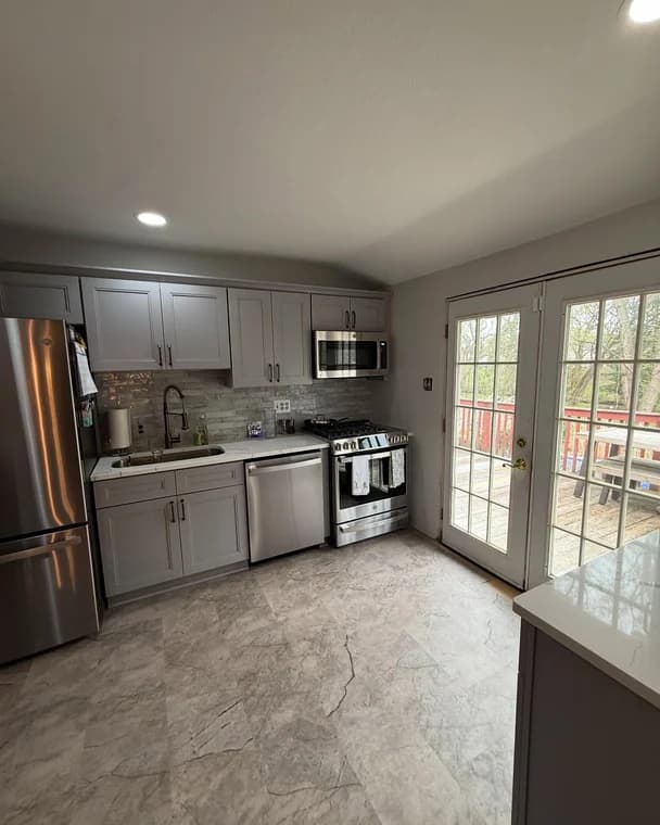A renovated kitchen with gray cabinets, stainless steel appliances, and tiled backsplash, finished with Bucci Paint’s professional interior services.