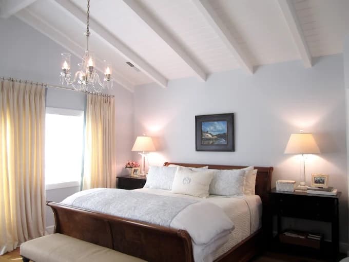 This is an image from Oliveira Painting Inc., located in Massachusetts. The photo shows a bright and elegant bedroom with light gray painted walls, white vaulted ceilings, and soft natural light enhancing the clean modern design.