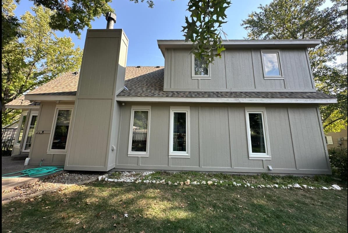This is an image from Painter's Painting. The image is a Neutral gray painted exterior on a two-story Kansas home with vertical siding and white window trim.