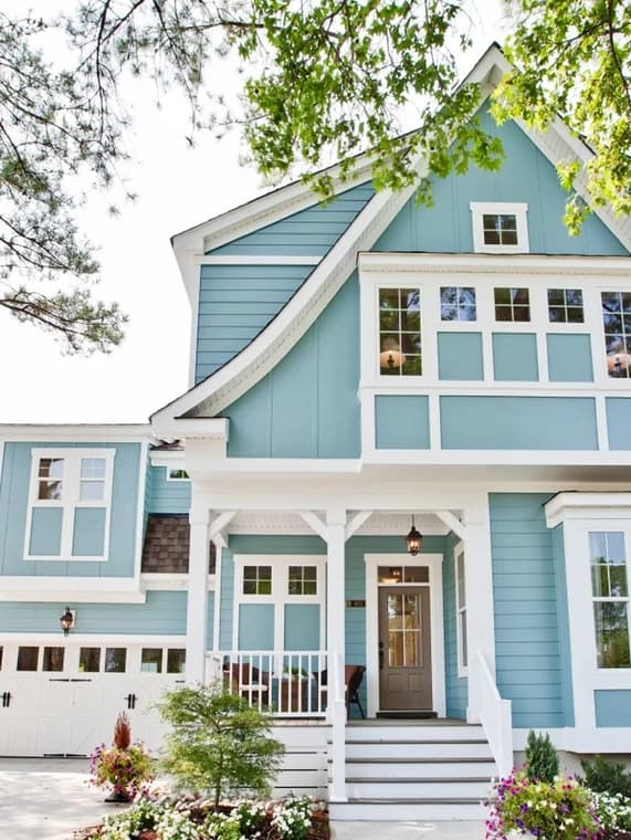 This is an image from Charlotte Pro Painters, located in North Carolina. This is a modern two-story home painted light blue with white trim, showing fresh exterior painting and a landscaped front yard.