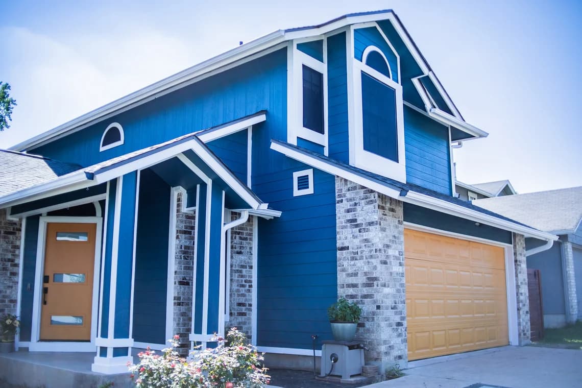 This is an image from That 1 Painter Austin, located in Texas. The exterior home photo features bold blue siding with white trim and a contrasting tan garage door.