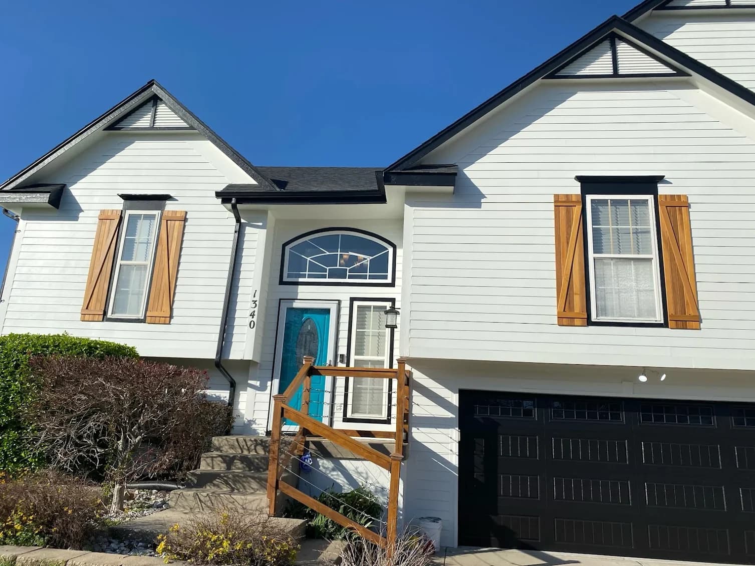 This is an image from Mission Painting and Home Improvements. The image shows a freshly painted exterior of a white home with black trim and natural wood shutters.
