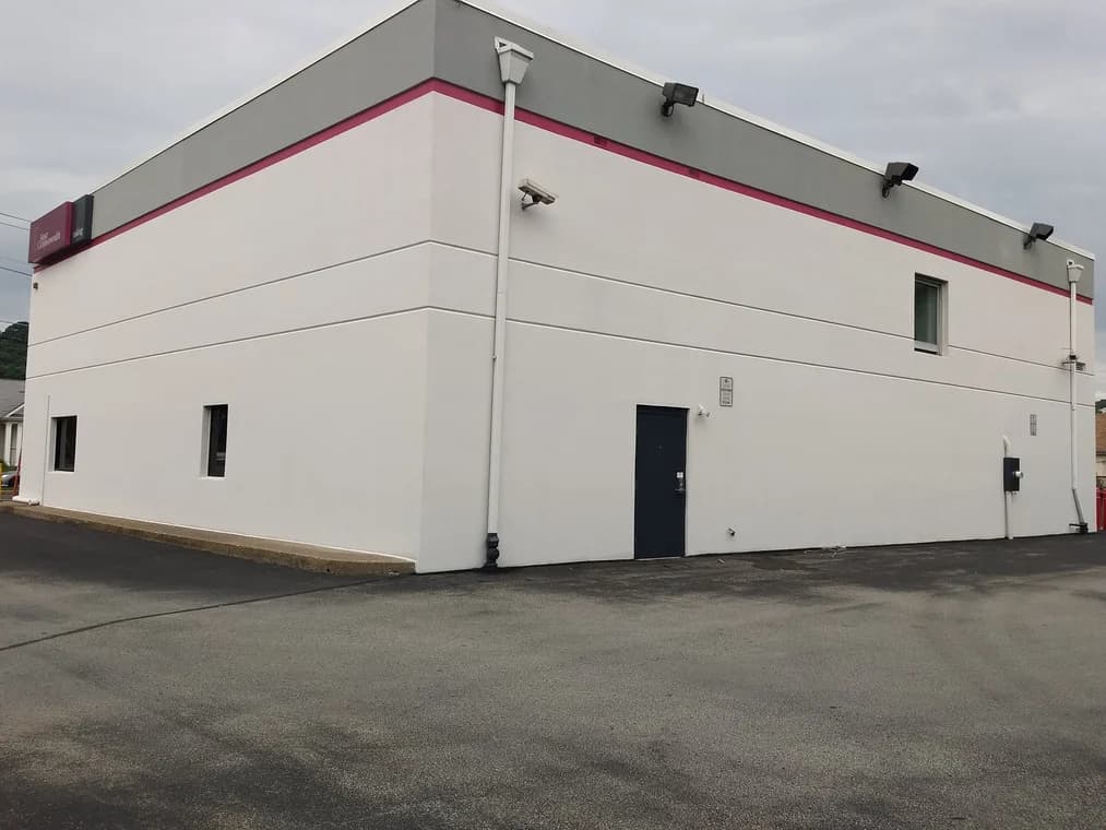 This is an image from Roman Paint Pros company, located in Penn Hills, PA. The image is a freshly painted commercial building with clean white walls, dark gray trim, and a red accent stripe, completed by Roman Paint Pros