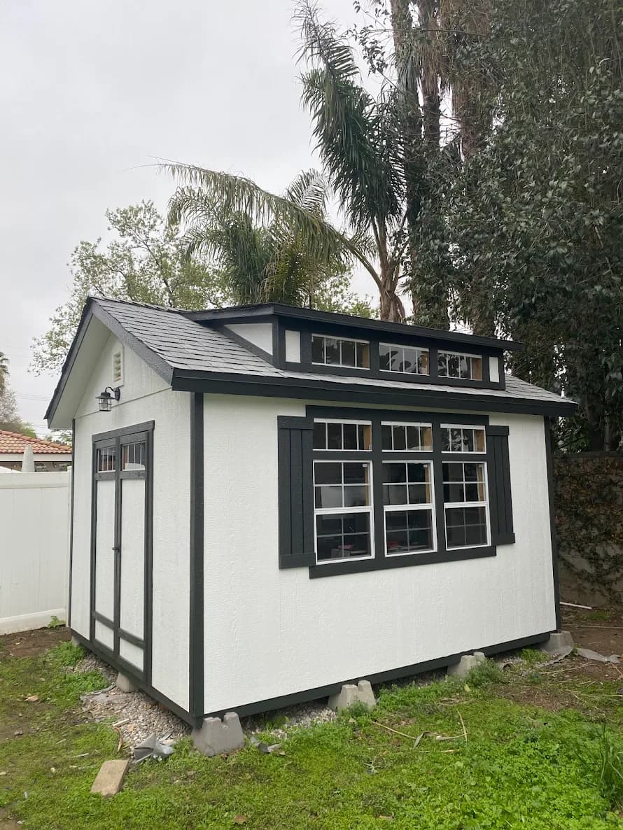 This is an image from ALLBRiGHT Painting, located in California. The image is from ALLBRiGHT Painting and shows exterior painting on a small white shed with black trim and multiple windows.