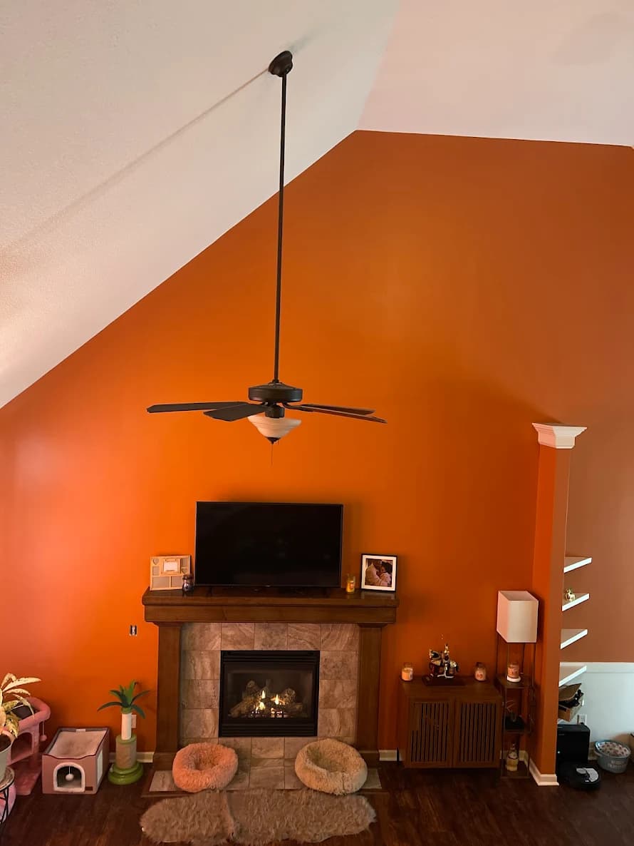 This is an image from Scarlett Painting & Remodeling. The image shows a living room with a tall feature wall painted in a bold orange color above a fireplace.