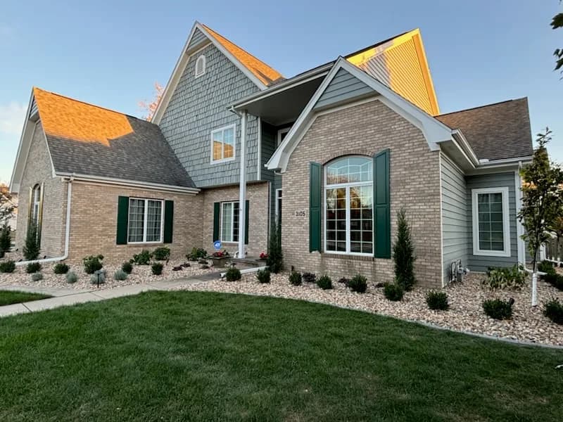Exterior painting by D J's Painting and Remodeling Inc in Bloomington, Illinois. The image shows gray siding, green shutters, brickwork, and white trim.
