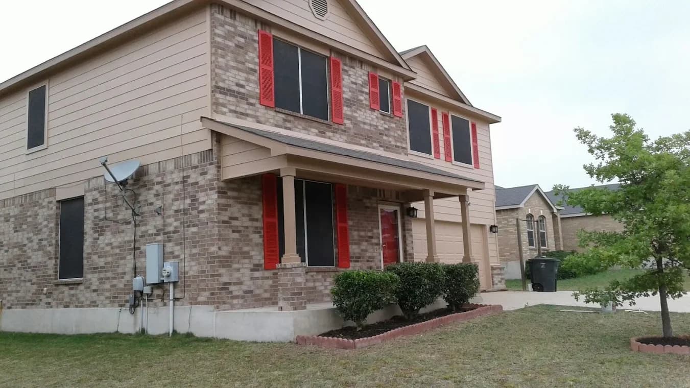 This is an image from Family Painting, located in Texas. The picture shows a repainted two-story home featuring tan siding, brick accents, and bright red shutters.