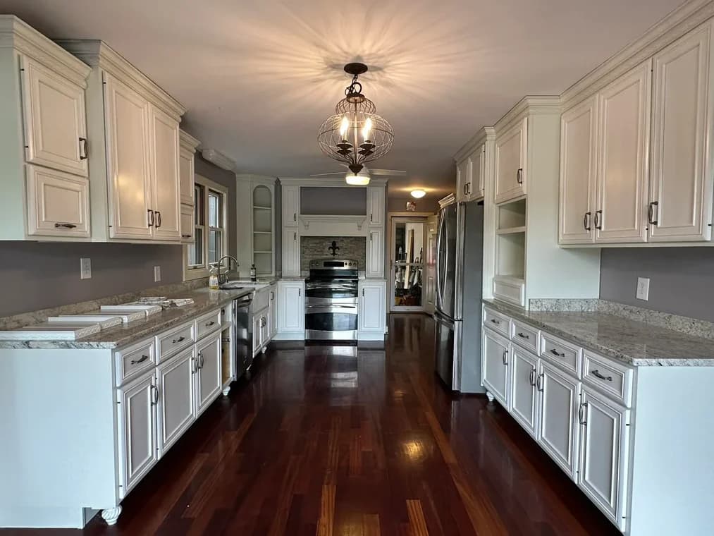 This is an image from Alarcon Pro Painting & Design, located in North Carolina. The interior photo features a modern kitchen with white cabinets, granite countertops, stainless steel appliances, and polished hardwood floors.