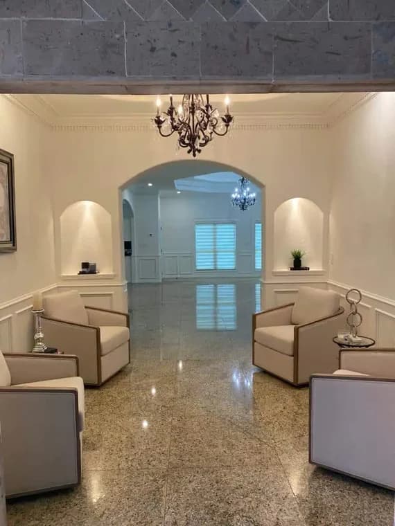 "This is an image from Armored Painting, located in Texas. The interior space shows a clean white sitting area with recessed wall niches, neutral chairs, and polished stone flooring leading into an open room."