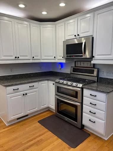 This is an image from That 1 Painter Knoxville, located in Tennessee. The image is a modern kitchen with white cabinets, granite countertops, and stainless steel appliances repainted by That 1 Painter Knoxville.