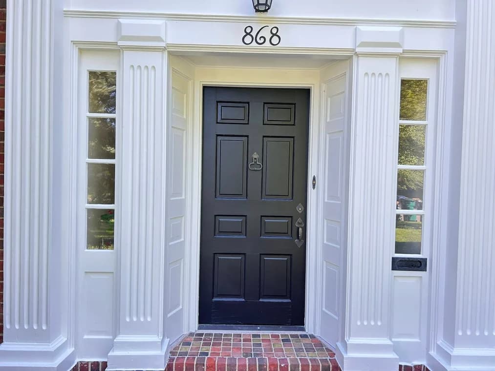 This is an image from AM Painting LLCcompany, located in Roseville, MI The image is a  refinished front entryway with freshly painted white trim and black door on a classic brick home by AM Painting in Grosse Pointe Park, Michigan.
