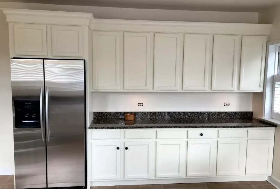 A freshly painted white kitchen with stainless steel appliances and white cabinetry. The space reflects a clean, modern look completed by Jordan's Painting LLC.