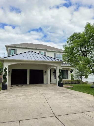 This is an image from Big Al's Painting, located in Texas. The photo shows a large two-story white brick home with a dark metal roof, arched entryway, and neatly maintained landscaping.