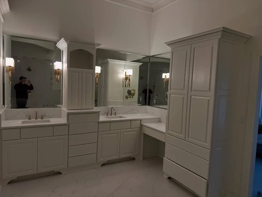 This is an image from Snap Painting Plus, located in Kentucky. The image shows a freshly painted bathroom with white cabinetry, marble-style countertops, large wall mirrors, and updated light fixtures.